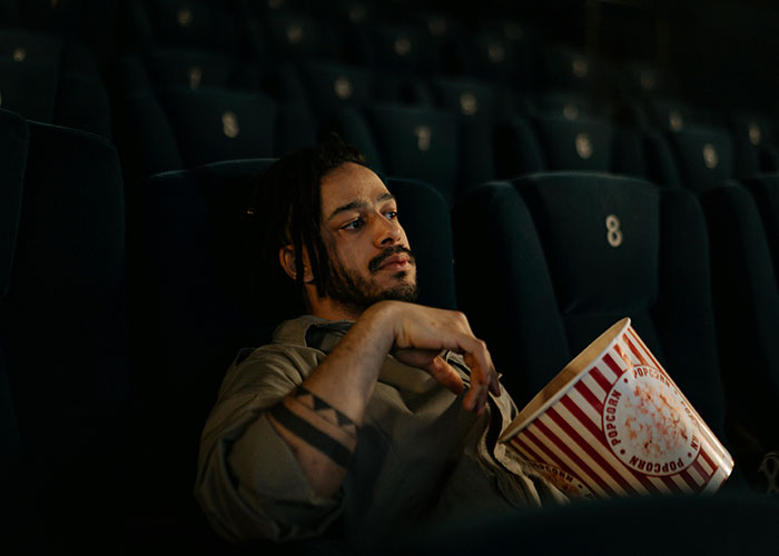 Man in an empty theater holding popcorn, possibly experiencing culture shock regarding early closing food places in Europe.