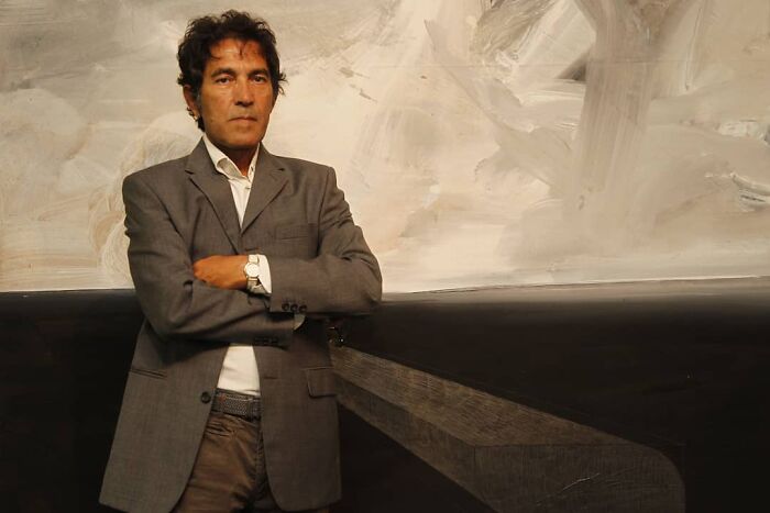 Man in a gray suit with arms crossed, standing in front of an abstract background, conveying a fresh perspective.