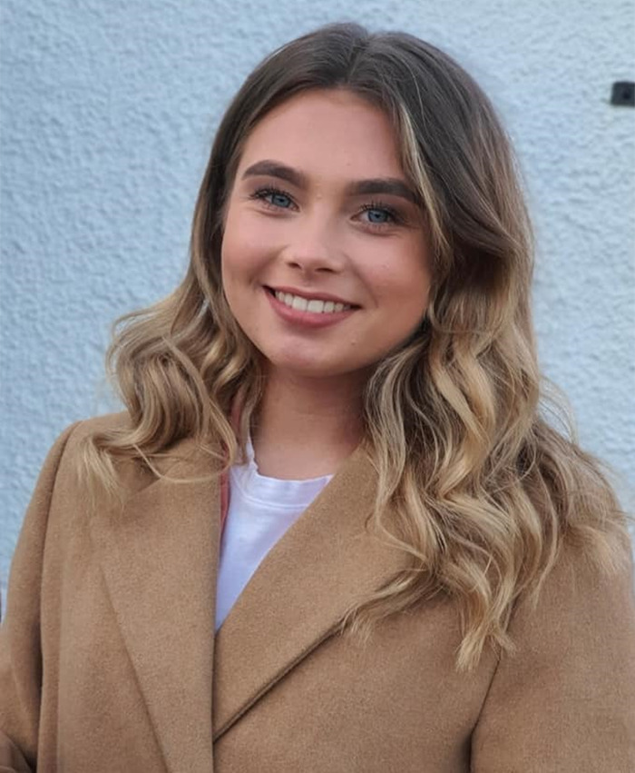 Young soldier smiling in a tan coat against a light background.