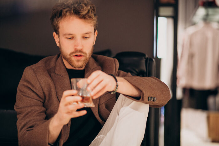 Man sitting on a sofa, holding a glass, reflecting on a first date experience.