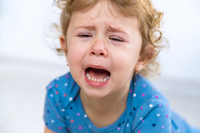 A toddler crying with tears, expressing a tantrum in a blue polka dot outfit.