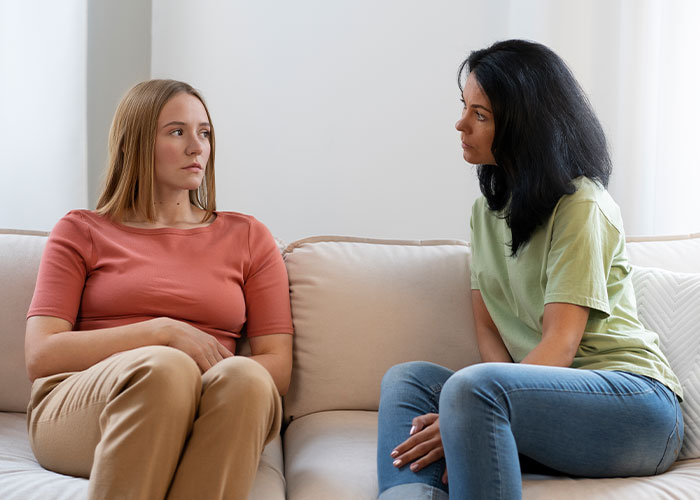 Two women sitting on a couch, having a serious conversation about being late.