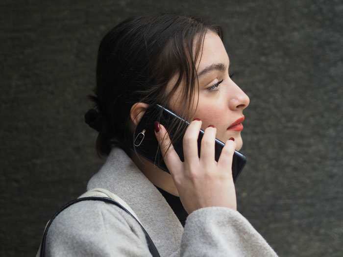 Woman in a coat talking on the phone, looking concerned, related to a discussion about leaving children home alone.