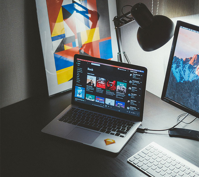 Laptop displaying music playlist, next to a colorful abstract art piece and a desktop monitor, highlighting tech and home decor.