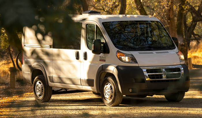 A white van parked on a sunlit dirt road in a forest setting.