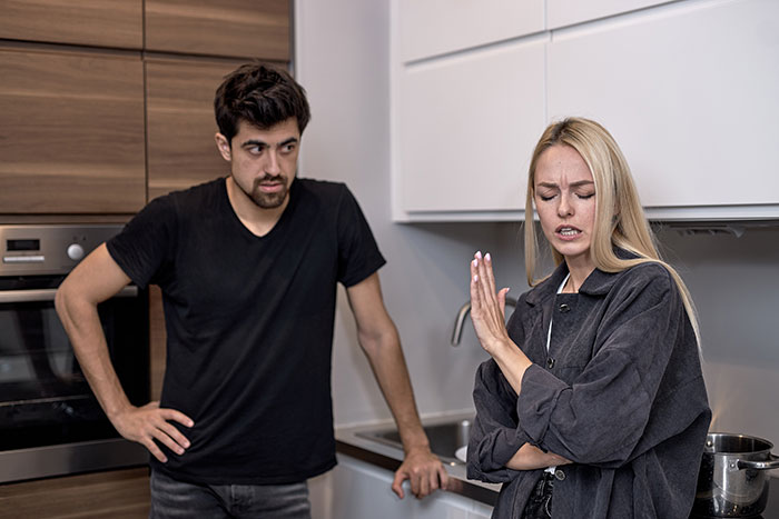 Man in a kitchen comments on laundry, woman reacts angrily, illustrating post-surgery relationship tension.