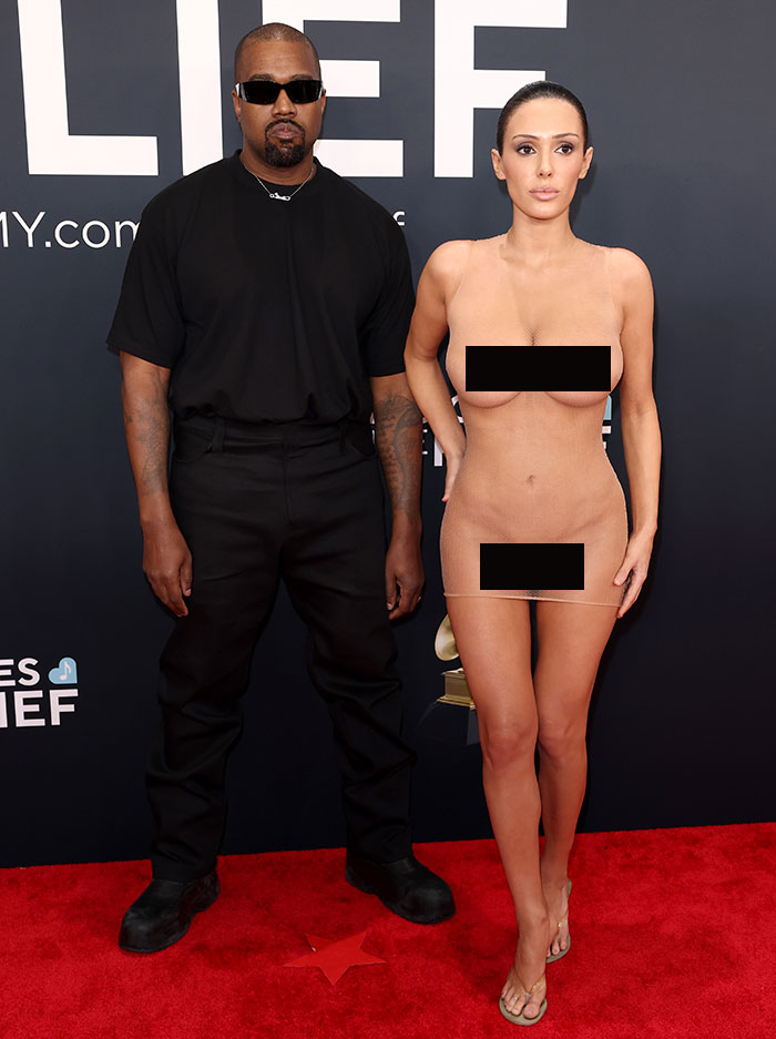 Two people on the red carpet, one in a black outfit, the other in a revealing outfit reflecting dress code discussion.