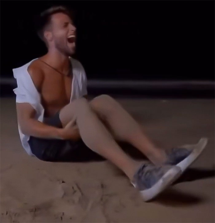 Man having a mental breakdown on a beach at night, sitting on the sand with a distressed expression.