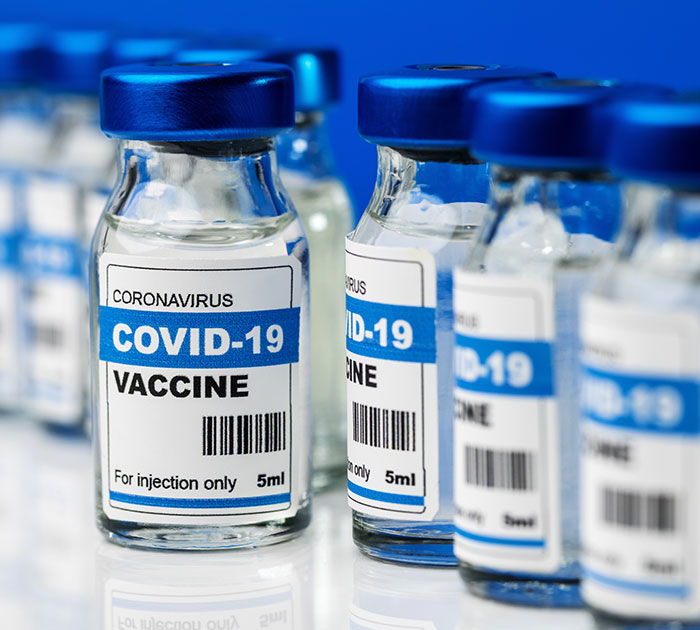 Covid vaccines vials with blue caps and labels, focus on foreground vial.