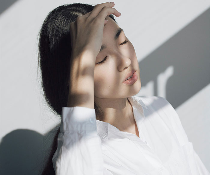 A woman in a white shirt, eyes closed, touching her forehead, reflecting on a fake wedding incident.