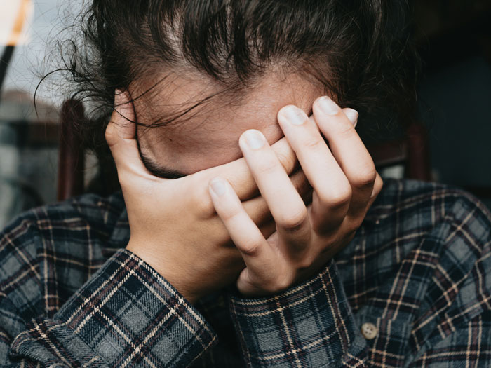 Woman covering face with hands, wearing a plaid shirt, reflecting emotional reaction to postpone wedding.