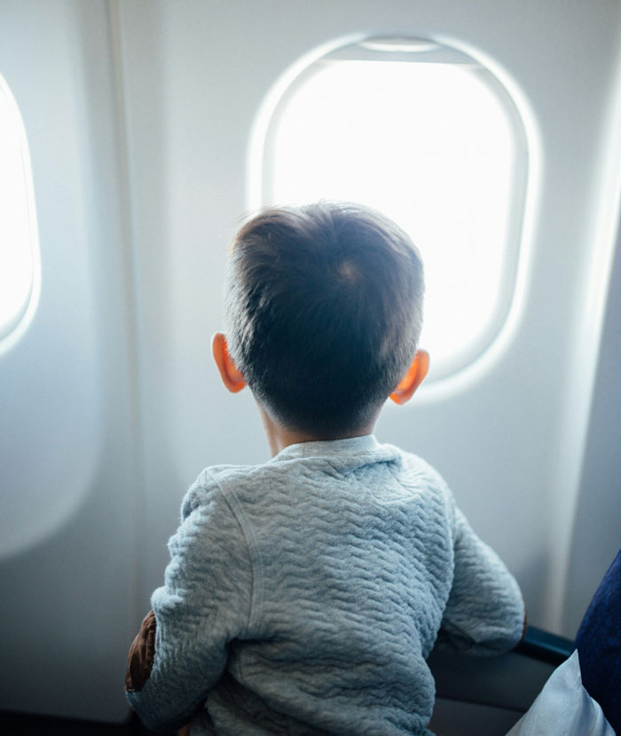 Child looking out an airplane window, related to babysit discussion.