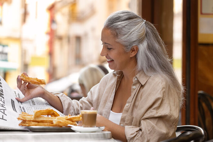 Woman enjoying churros and coffee, sitting at a cafe table, reading a newspaper about worst first dates.