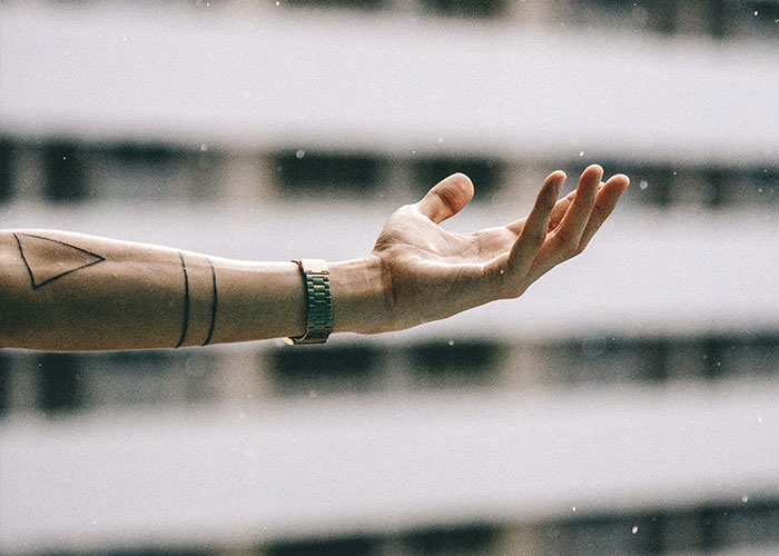 Tattooed arm extended in the rain, showcasing minimalist ink design on forearm.