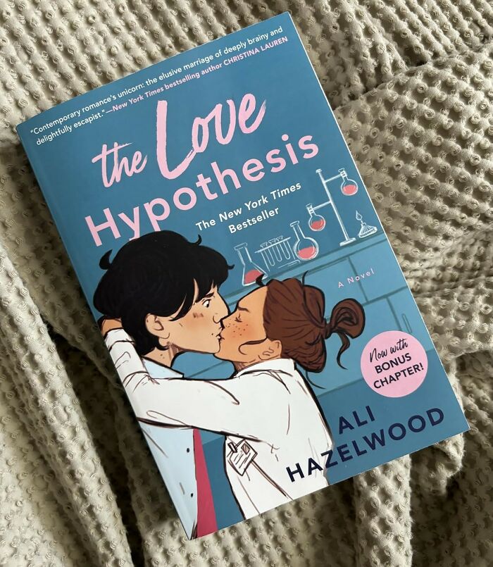 "The Love Hypothesis book cover on a cozy blanket, showcasing romantic themes."