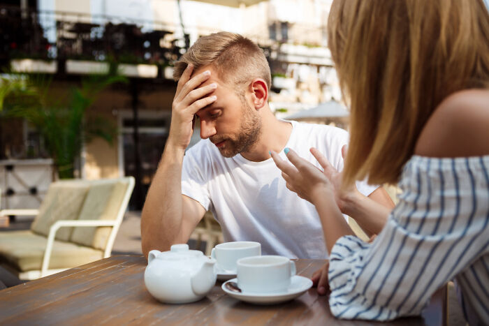 Man looking frustrated on a bad first date, sitting at an outdoor cafe table with tea set.