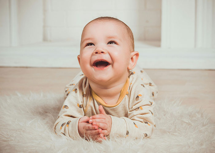 Smiling baby on a soft rug, wearing a patterned onesie, embodying wholesome comfort.