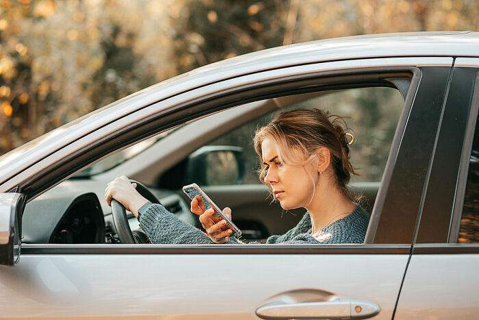 Woman in a car checking her phone, conveying a sense of disappointment on a date.