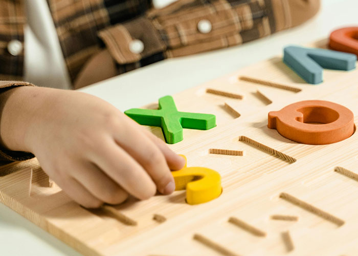 Child's hand playing with colorful puzzle pieces on a wooden board, symbolizing wholesome activities.