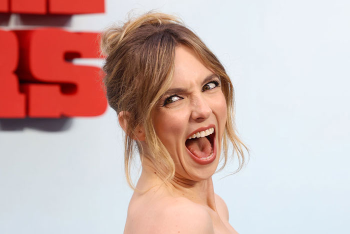 Jodie Comer, actor from 28 Years Later cast making a dramatic expression at an event with a white and red background.