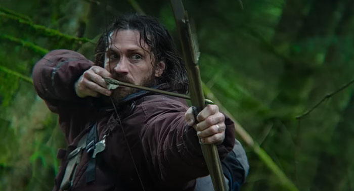 Aaron Taylor-Johnson, actor with a bow and arrow in a forest scene, related to the 28 Years Later cast.