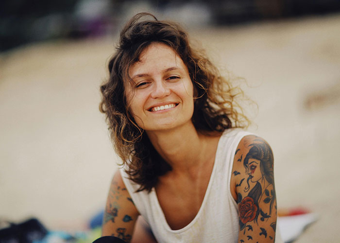 Person smiling on a beach, showing colorful tattoos on their arms, highlighting inked designs.