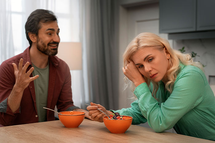 Man gesturing while speaking to woman with cereal at table, highlighting relationship tension.