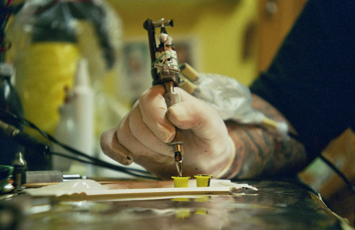 Tattoo artist's gloved hand holding a tattoo machine, preparing ink in a studio setting.