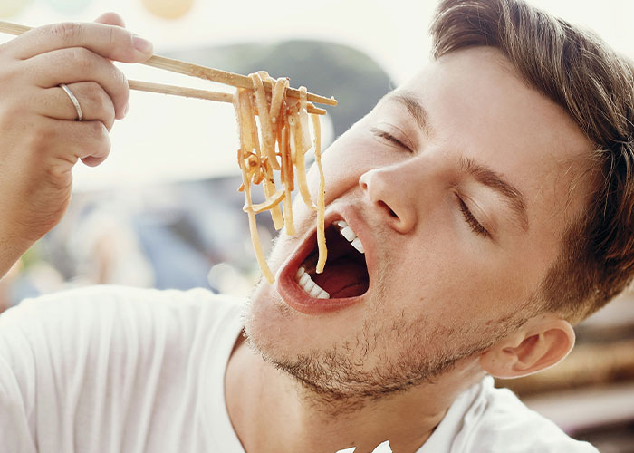 Man eating spicy food with chopsticks, eyes closed, enjoying the meal.