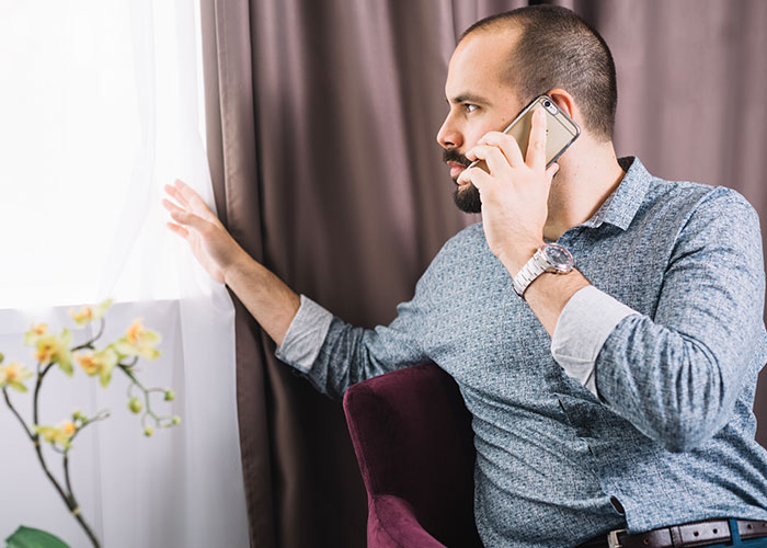 Man on phone near window; concerned expression discussing driveway issue involving mom with dementia.