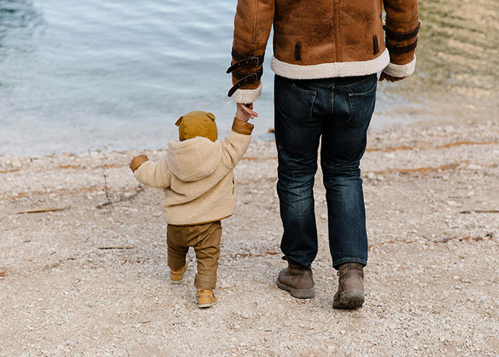 Adult and child holding hands by the water, illustrating young people and affordability concerns for having kids.