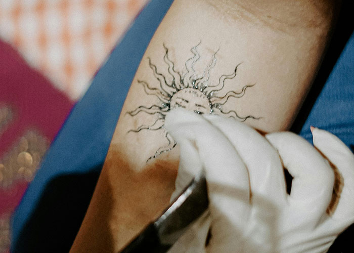 Tattoo artist inking a sun design on a person's arm using a tattoo machine.