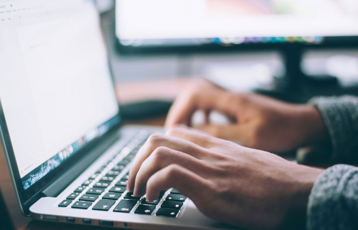 Hands typing on a laptop keyboard, related to Lithuanian man and fake invoice story.