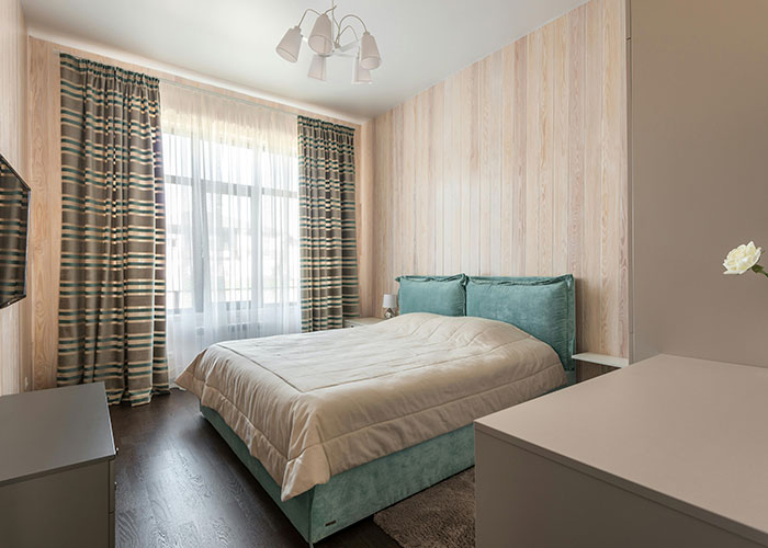 Modern European bedroom with teal bed and patterned curtains, highlighting culture shocks in home decor.