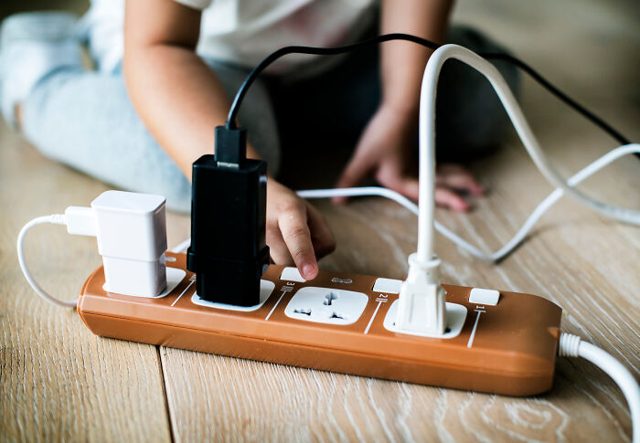 Child using a power strip on wooden floor, showcasing travel must-haves for efficient packing.