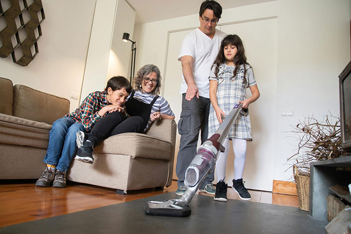 Family in living room as a child vacuums, highlighting the topic of parents and chores without payment.