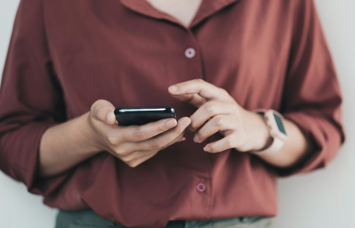 Woman in a red shirt using a smartphone, with a focus on hands and a smartwatch for communication.