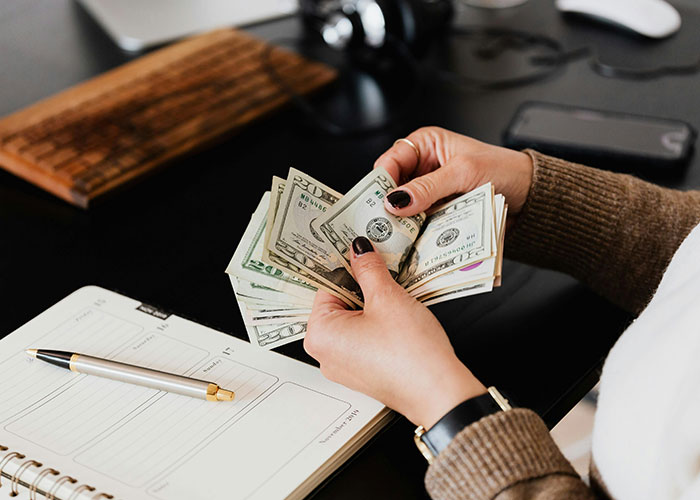 Person counting money with a notebook and pen, highlighting affordability concerns for young parents.