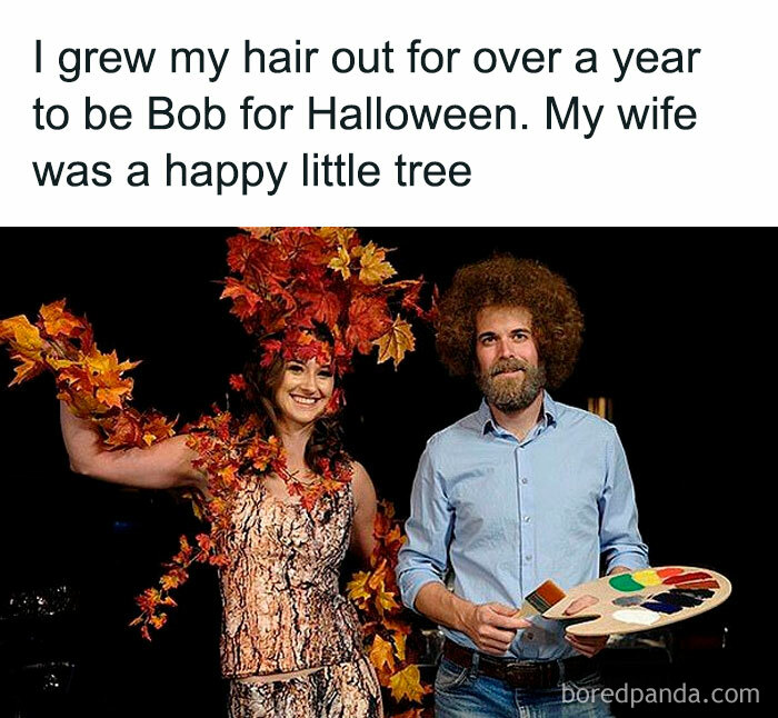 Couple in creative Halloween costumes, one as Bob Ross and the other as a tree, embodying heartwarming memes and joy.