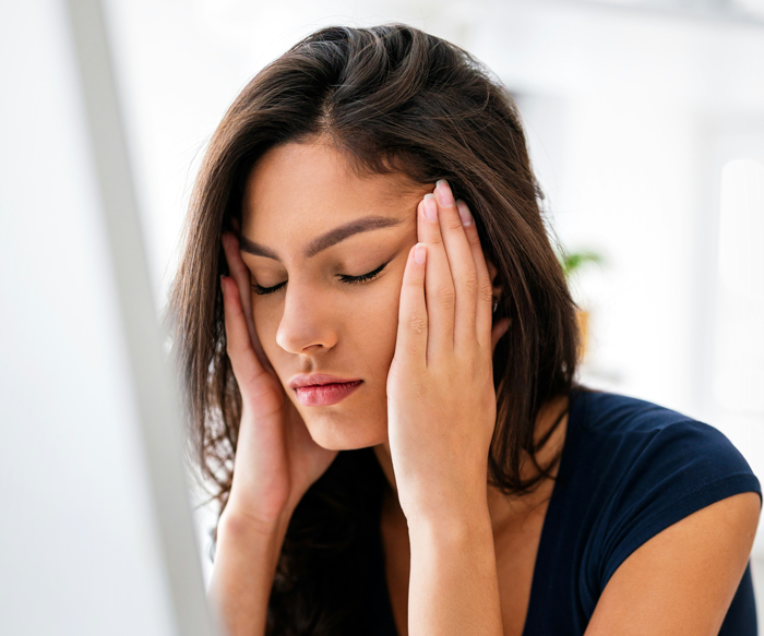 Woman looking stressed, eyes closed, and holding her head, reflecting tension regarding a tattoo reveal situation.