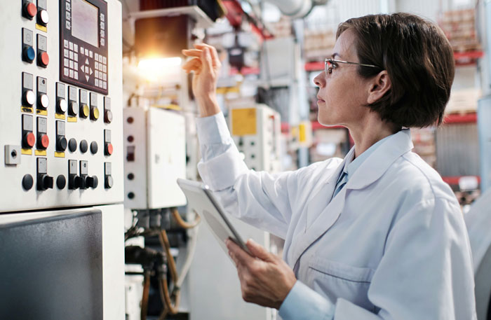 Woman engineer in lab coat operates machinery, showcasing engineering expertise.