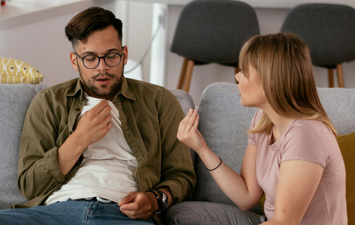 A couple having an intense conversation on a couch, focused on husband denying leaving small children home alone.