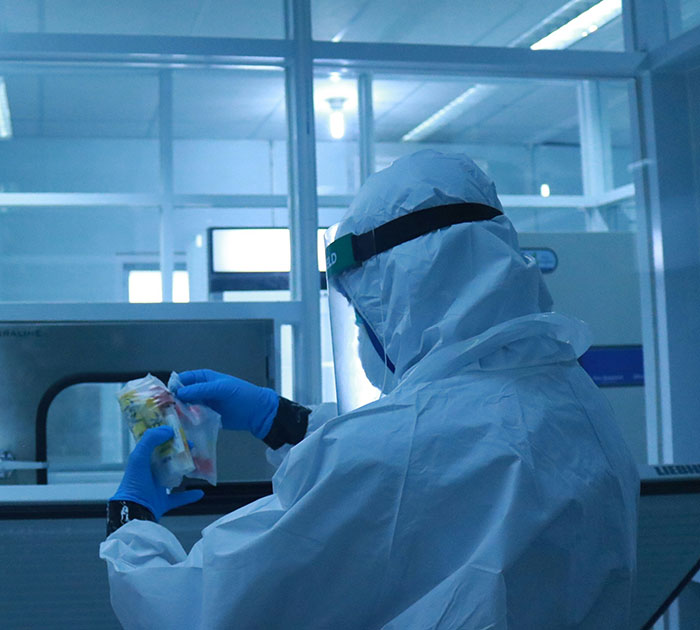 Scientist in protective gear examining specimen in lab related to Covid vaccines and syndrome research.