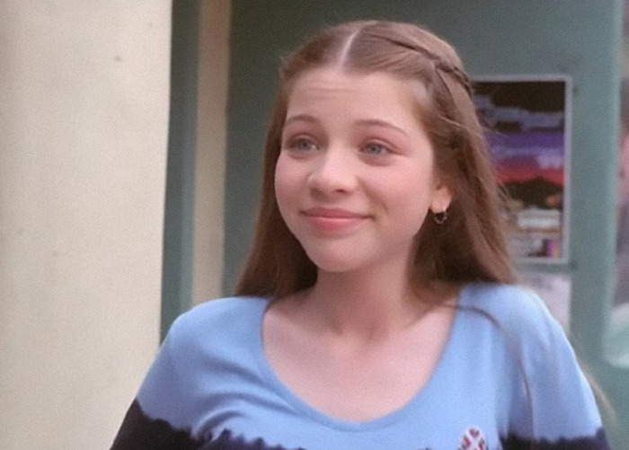 Michelle Trachtenberg with braided hair and a blue shirt smiling.