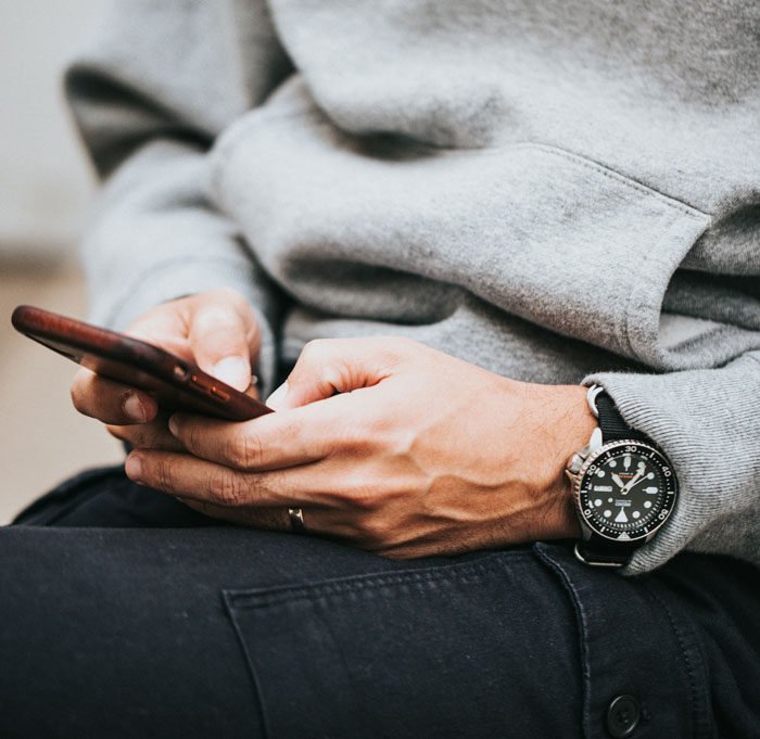 Person in a grey sweater holding a phone, focusing on a wristwatch. Vegan family dynamics concept.