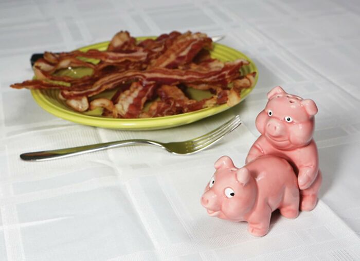 Funny Valentine's Day gift idea: pig salt and pepper shakers with a plate of bacon in the background.