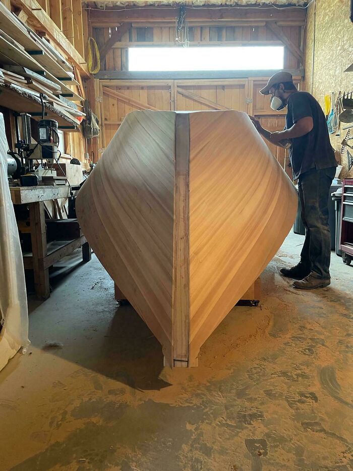 Craftsman working on an impressive woodworking project, constructing a wooden boat in a workshop.