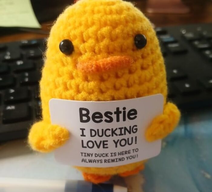 Yellow knitted duck holding a funny Valentine's Day card reading, "Bestie, I Ducking Love You," in front of a keyboard.