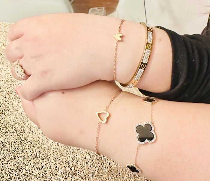 Two wrists adorned with Galentines Day gifts: gold heart and clover charm bracelets, and a diamond-studded bangle.