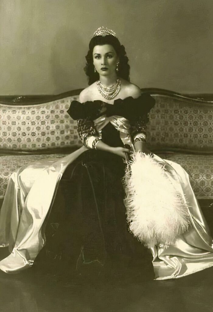 Woman in an elegant historical gown with a tiara and jewelry, sitting on a vintage sofa, highlighting rare historical photos.